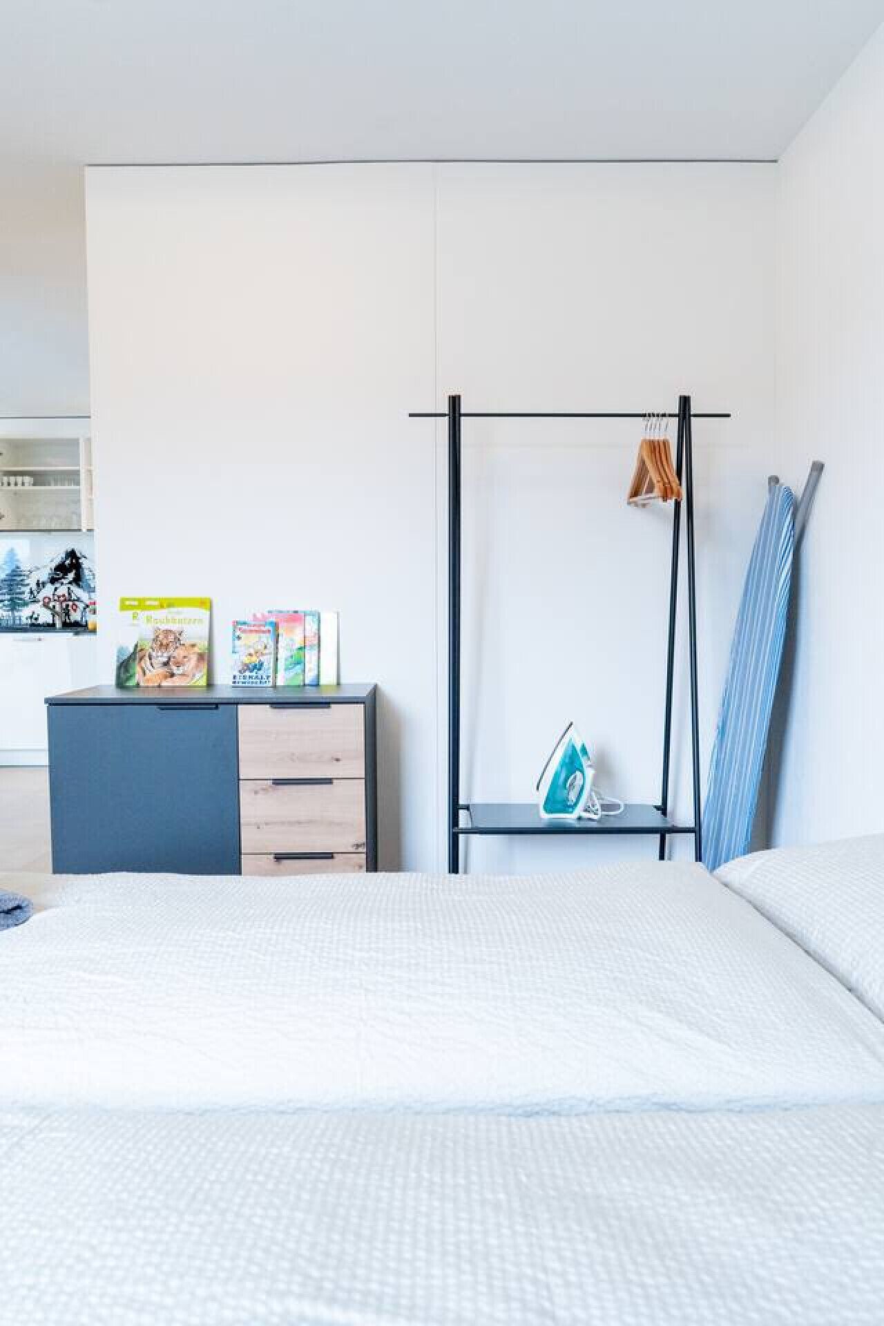Ein modernes Schlafzimmer mit einem Bett, einem Schminktisch, einem Kleiderschrank und einer Kleiderstange mit Kleidung und einem Handtuch.