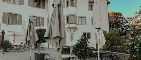 Une cour avec des sièges en plein air, un bâtiment blanc surmonté d’une tour et un ciel dégagé.