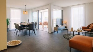 A modern living room with a sofa, a dining area with chairs, a coffee table, and a TV. - Apartment Eiger with lake and mountain view (Spiez)