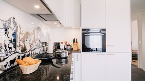 A modern kitchen with white cabinetry, a stainless steel refrigerator, and a black countertop. - Apartment Mönch near lake and mountains (Spiez)