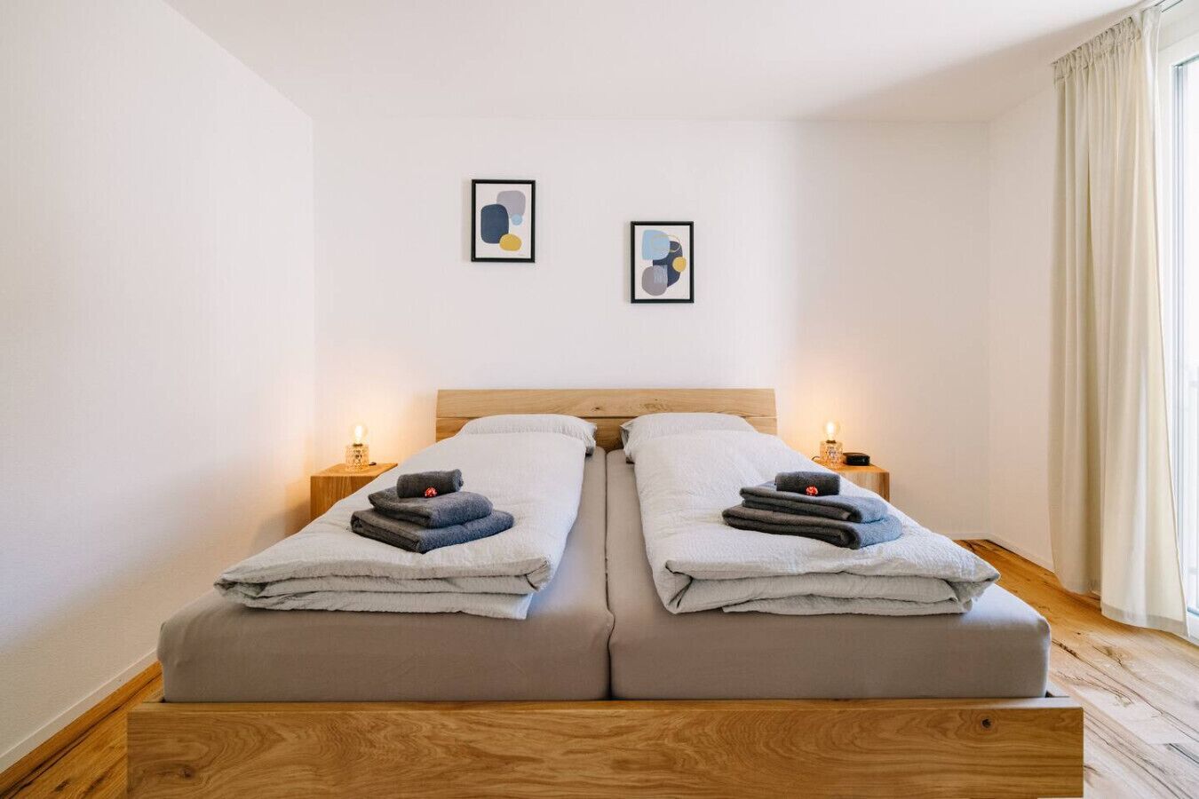 A double bed with two bedside tables, each with a lamp. There are two framed abstract paintings on the wall.