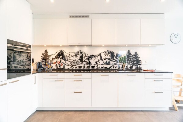 Una cocina moderna con armarios blancos, una isla central con cajones y un salpicadero decorado con una escena de montaña.