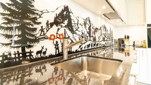 Una cocina moderna con un lavamanos de acero inoxidable, una encimera reflectante y un mural que muestra un paisaje montañoso con banderas suizas.