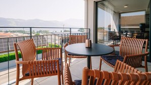 Un balcón con mobiliario de mimbre y una mesa, con vistas a un paisaje urbano y montañas.