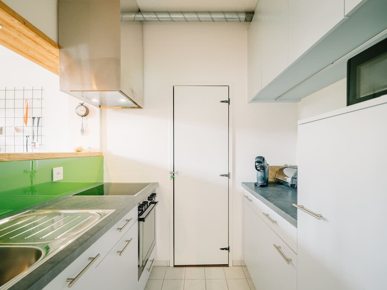 A compact kitchen with a stainless steel sink, a stove, and a microwave. There is a green countertop and white cabinets.