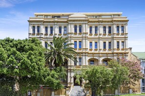 Un edificio grande e histórico de varios pisos, con una entrada central escalonada y una fachada simétrica.