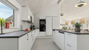 Une cuisine moderne avec des meubles blancs, un four encastré et un lave-vaisselle. Une fenêtre se trouve sur le côté gauche et un espace pour l’évier sur le côté droit.