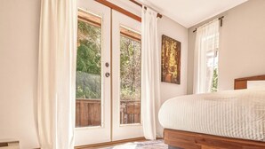 A bedroom with a bed, a large window with curtains, a wooden headboard, and a rug. - Tonquin Beach House - Wood Fireplace | EV Charger | Steps from Beach I Tofino (Tofino)