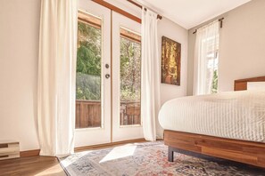 A bedroom with a bed, a large window with curtains, a wooden headboard, and a rug. - Tonquin Beach House - Wood Fireplace | EV Charger | Steps from Beach I Tofino (Tofino)