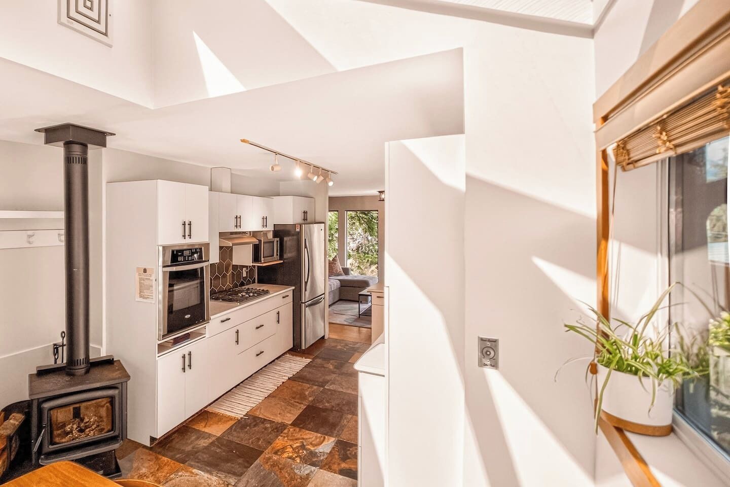 Een moderne keuken met witte kasten, een houtkachel en uitzicht op een eetgedeelte.
