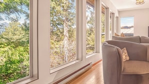 A room with large windows, a sofa, and a ceiling light fixture. - Tonquin Beach House - Wood Fireplace | EV Charger | Steps from Beach I Tofino (Tofino)
