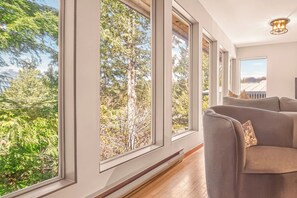 A room with large windows, a sofa, and a ceiling light fixture. - Tonquin Beach House - Wood Fireplace | EV Charger | Steps from Beach I Tofino (Tofino)