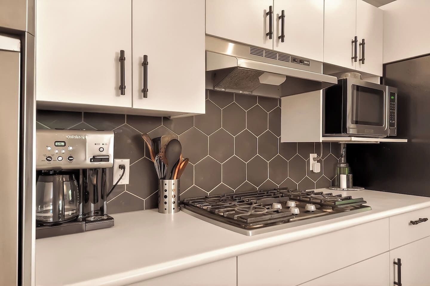 A modern kitchen with a coffee maker, microwave, stove, and utensil holder.