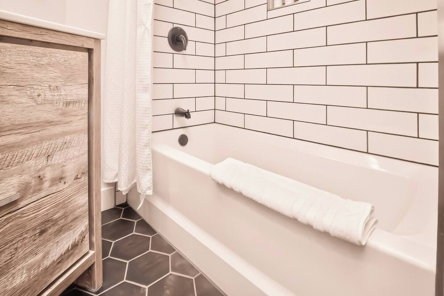 A bathroom with a white bathtub, a wooden cabinet, and hexagonal patterned tiles.