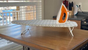 Una cocina con encimera de madera, una tabla de planchar con un plancha naranja y una ventana con persianas.