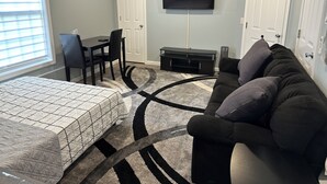 A bedroom with a bed, a desk, a chair, a TV, and a couch.