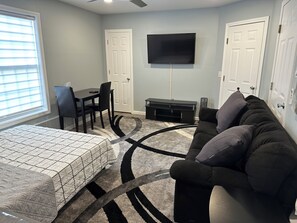 A bedroom with a bed, a desk, a chair, a TV, and a couch.