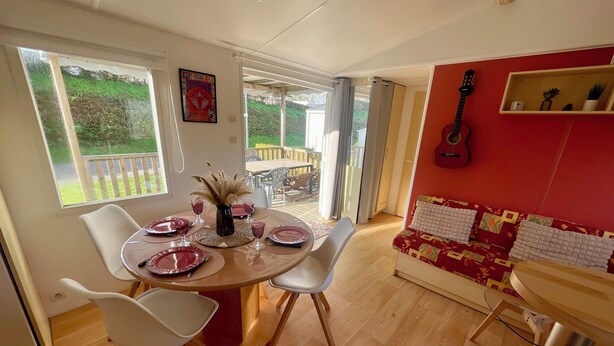 Un coin repas avec une table ronde pour quatre personnes, des chaises blanches et un mur rouge orné d’une guitare.
