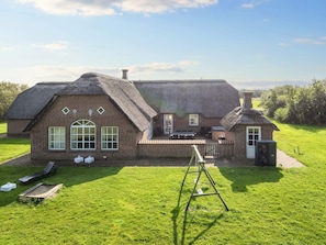 A traditional brick house with a thatched roof, a small attached structure, and a grassy yard with a wooden swing set. - 4 Star Holiday Home in Ulfborg (Ulfborg)