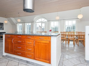 A spacious kitchen with a large island, wooden cabinets, and a dining area with chairs. - 4 Star Holiday Home in Ulfborg (Ulfborg)