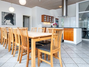 A dining area with a wooden table and chairs, a kitchen with cabinets and appliances, and a large window. - 4 Star Holiday Home in Ulfborg (Ulfborg)