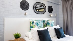 A neatly made bed with white and dark blue pillows, a small wooden nightstand with a plant, and two wall-mounted mirrors above it. - Batemans Bay Studio Escape With Lush Vista (Batehaven)
