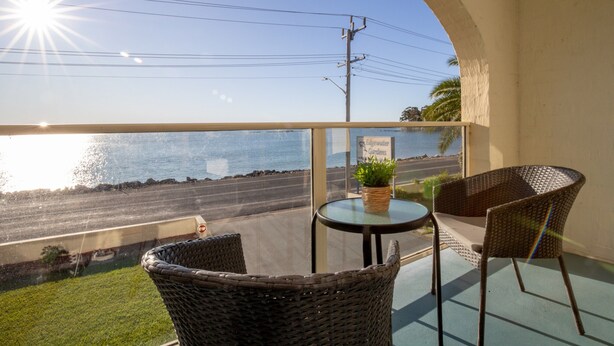 A balcony with wicker chairs, a small table, and a potted plant. - Batemans Bay Studio Escape With Lush Vista (Batehaven)