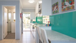 A modern kitchen with a green backsplash, white cabinets, and a large island. There are two wall-mounted ovens and a refrigerator. - Batemans Bay Studio Escape With Lush Vista (Batehaven)