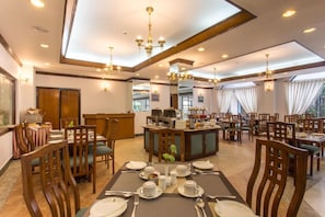 A hotel dining area with multiple tables set for breakfast, a central counter with a coffee machine, and a large window providing natural light. - Hotel Le Himalaya (Kathmandu)