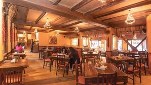 A restaurant with wooden tables and chairs, a high ceiling with exposed beams, and hanging light fixtures. - Hotel Roadhouse (Kathmandu)
