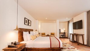 A hotel room with a large bed, bedside tables, a desk, a chair, a television, and a patterned rug. - Hotel Roadhouse (Kathmandu)