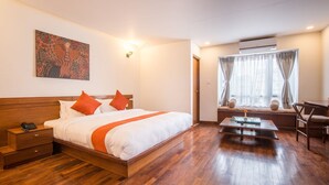A hotel room with a wooden bed, a bedside table with a phone, a nightstand, a small table with a vase, a chair, and a window with curtains. - Timber House (Kathmandu)