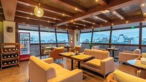 A cozy lounge area with sofas and tables, a Coca-Cola vending machine, and large windows offering a city view. - Timber House (Kathmandu)
