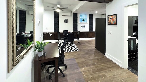 Een modern interieur met een houten vloer, een eethoek met een zwart-wit gestreept tapijt, een grote spiegel en een plafondventilator.