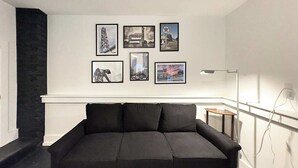 Een moderne woonkamer met een zwart hoekbank, een open haard en een verzameling ingekaderde foto's aan de muur.