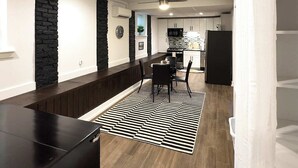 Een moderne keuken met witte kasten, een zwarte koelkast en een eethoek met een zwart-wit gestreept vloerkleed.