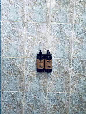 Dos botellas de champú de oliva y jabón líquido sobre una pared de baldosas.