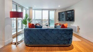 Ein modernes Wohnzimmer mit einem blauen Sofa, roten und blauen Kissen, einer roten Stehlampe und einem großen Fernseher an der Wand.
