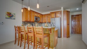 A kitchen with wooden cabinets, a central island with bar stools, a microwave, and a refrigerator.