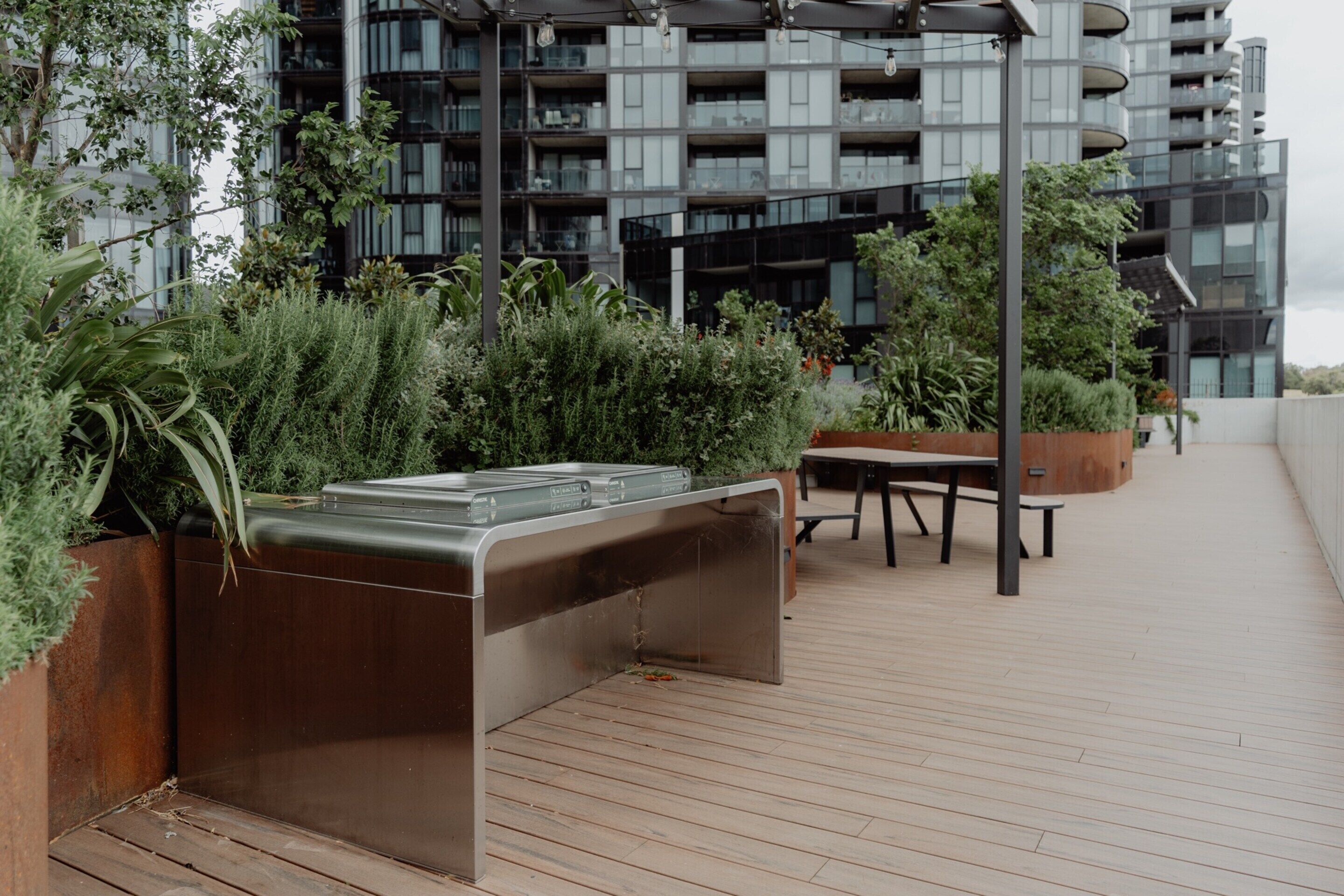 A rooftop terrace with a built-in barbecue, wooden flooring, and potted plants.