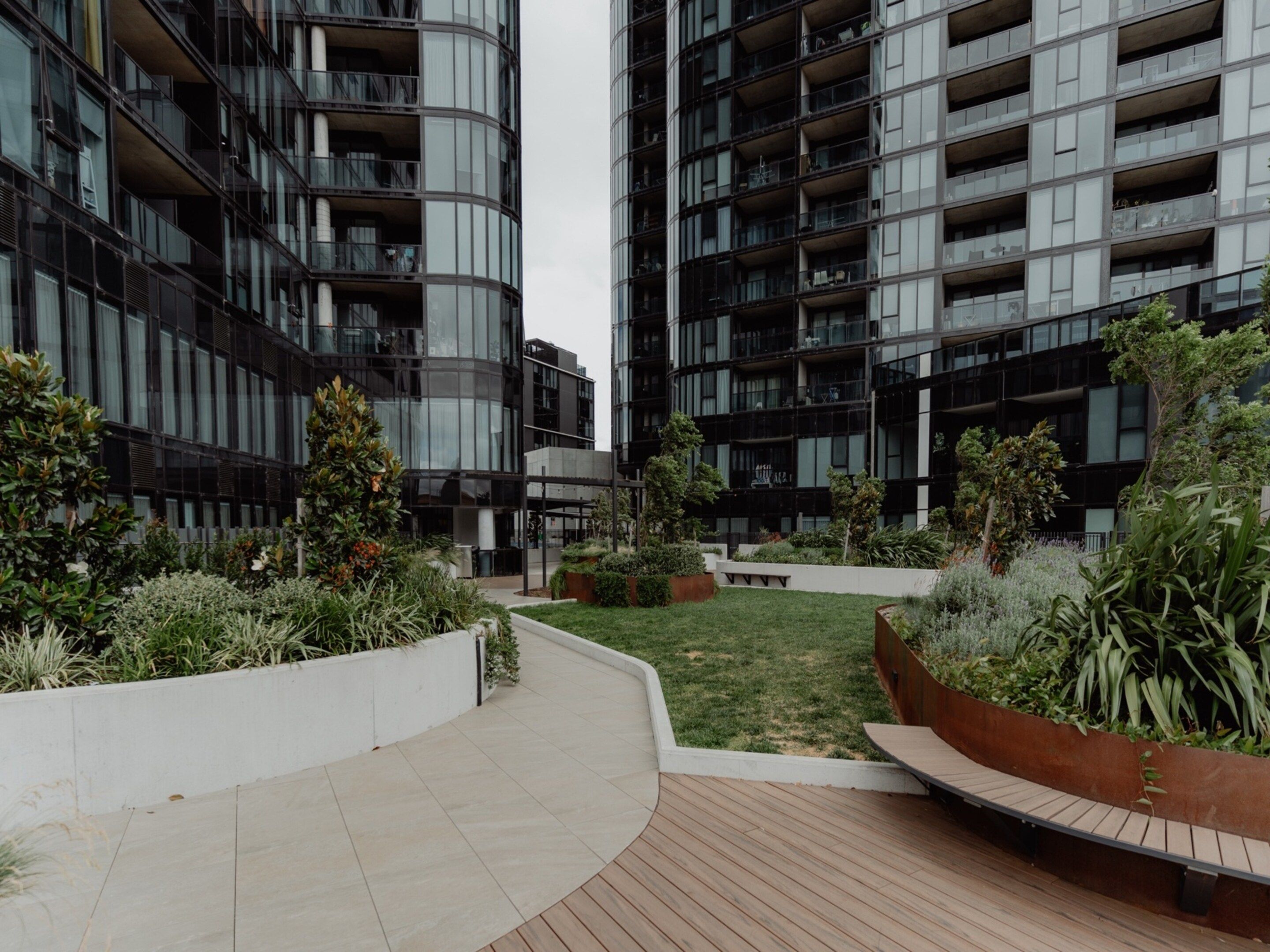 A modern building with multiple balconies and a landscaped courtyard with planters and a wooden deck.