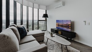 En moderne stue med et stort fladskærms TV, en sofa, et sofabord og en gulvlampe.