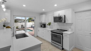 A modern kitchen with white cabinets, a stainless steel stove, and a microwave. - Stylish 4BR Oasis | Heated Pool, Spa & Fire Pit (Pompano Beach)