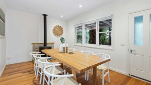 Un coin repas avec une table en bois et des chaises blanches, une cheminée en pierre et une fenêtre donnant sur la forêt.