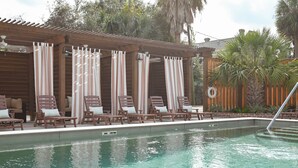 Zona de piscina con sillones de descanso y cortinas a rayas.