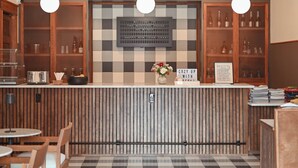 Una cafetería con suelo a cuadros, muebles de madera y una barra central con un letrero que dice 'COZY UP WITH'.