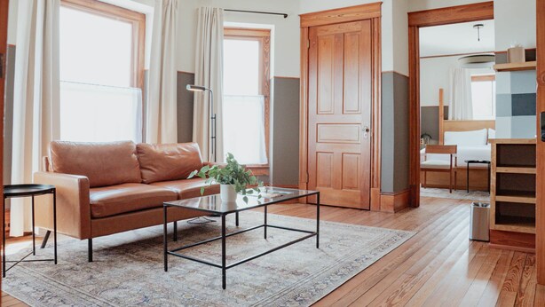 Ein großzügiges Wohnzimmer mit einer Ledersofa, einem Glastisch und einem großen Fenster mit Vorhängen.