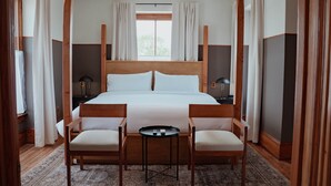 Ein Hotelzimmer mit einem großen Bett, zwei Holzsesseln, einem kleinen Tisch und einem Nachttisch mit einer Lampe.