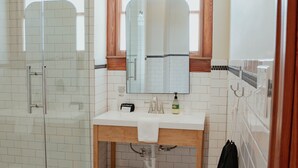 Ein Badezimmer mit Duschkabine aus Glas, einem weißen Waschbecken und einem Badezimmerunterschrank aus Holz sowie einem Schachbrettfußboden.