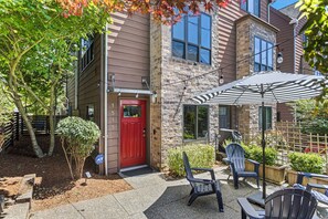 A building with a red door, outdoor seating with chairs and an umbrella, and a small garden area. - Green Lake Modern K/Q  + Parking | Stadium Access (Seattle)